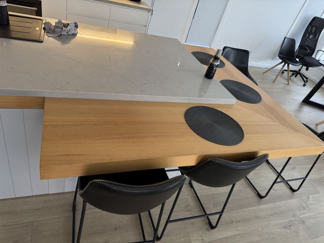 The same island up close: white stone over a warm oak breakfast bar, black stools.