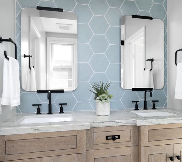 Double vanity in oak with a marble top, pale blue hexagon tiles and black fittings.