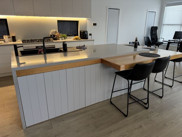 Your friends' island: white V-groove panelling, an oak band under the stone, a black double sink.