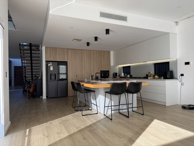 Your friends' kitchen: the oak wall to the ceiling, a fridge niche, the L-shaped oak bar and black stools.