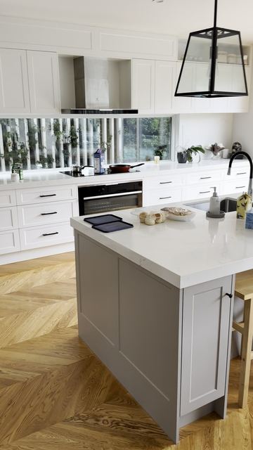 A white shaker kitchen on a herringbone oak floor: black handles and cage pendants over the island.