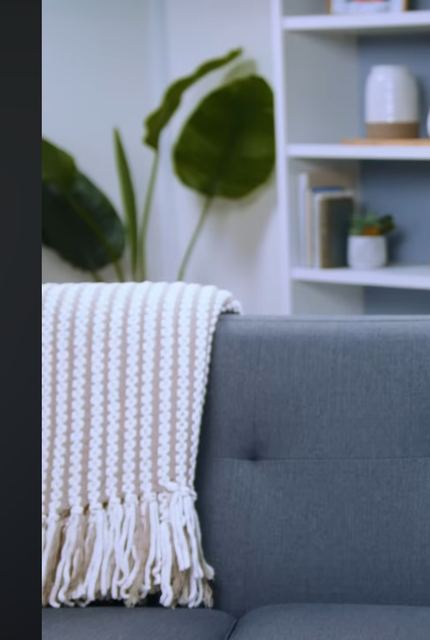 A grey sofa with a chunky knit throw, a plant and white shelving.