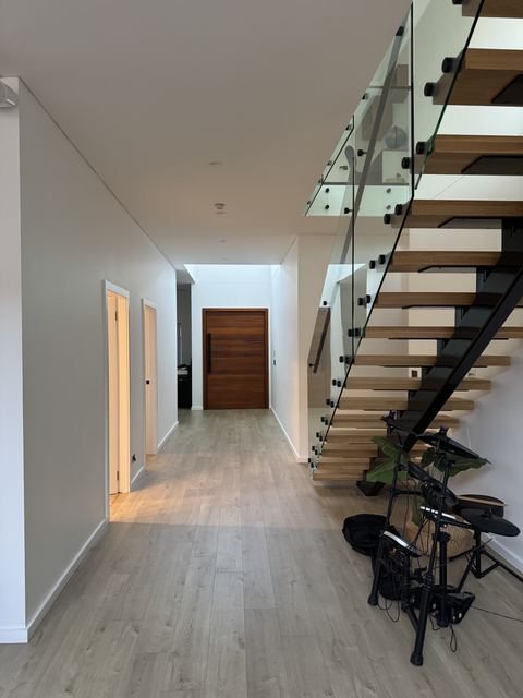 Your friends' hall: an open oak stair with a glass balustrade and an oak front door at the end.