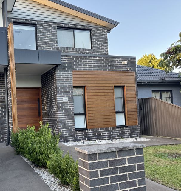 Your friends' house from the street: dark brick, a timber-clad bay and a vertical-grain timber door.